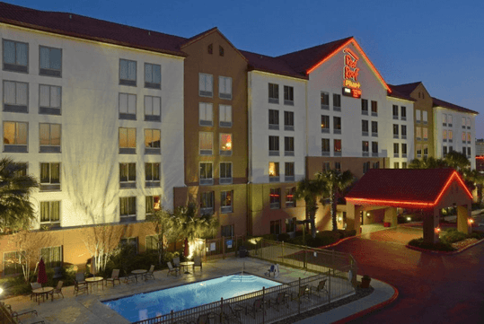 Beautifully landscaped entrance to the hotel with the hotel sign and view of the outdoor pool.