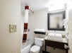 Compact bathroom with a bathtub and shower, red and white striped curtain, toilet, sink with countertop, wall mirror, towel rack, and wall-mounted light.
