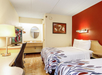 Hotel room with two beds, a desk, a wall-mounted TV, and a round mirror above a sink. One wall is red.