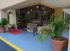 Entrance with a bench, potted plants, red doormat, and glass doors leading inside a brick building.