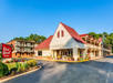 Exterior view of a Red Roof Inn with a distinctive red roof, surrounded by greenery and a clear blue sky.