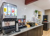 Drink station with juice dispenser, coffee machine, and breakfast foods on a countertop.