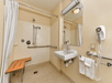Accessible bathroom with a walk-in shower, a mounted showerhead, a bench, grab bars, a wall-mounted sink, a mirror, and a hair dryer.