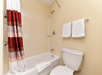 Bathroom with a white bathtub and shower, a toilet, a red and white striped curtain, and two white towels hanging on the wall.