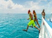 Two people in snorkel gear jump off a boat into turquoise ocean waters, with others watching and taking photos.