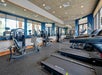 Modern gym with treadmills, weight machines, and large mirrors on the walls; windows provide natural light.