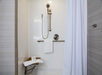Accessible shower with a mounted showerhead, grab bar, wooden bench, white towel, and a white curtain.