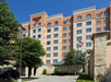 A multi-story Residence Inn by Marriott hotel building with arched windows, an American flag, and trees in the foreground on a sunny day.