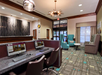 Hotel lobby featuring a computer workstation, reception desk, armchairs, and large windows by the entrance. The space has modern lighting and patterned carpeting.