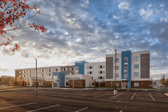 Wide shot of the blue, white, and gray front exterior of the Residence Inn by Marriott Columbus Airport with the sunset shining on it.