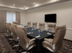 A conference room with a long table, eight brown chairs, a large screen on the wall, and bottles of water on the table.
