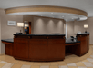 Hotel reception desk with wooden counters, black countertops, two lamps, and a sign on the wall.