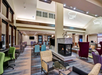 Modern hotel lobby with a central fireplace, colorful seating, tables, high ceiling, and abstract light fixtures.