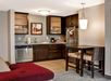 A modern kitchenette with dark cabinets, stainless steel appliances, a small dining area, and a red cushioned loveseat. A framed picture hangs on the wall above the countertop.