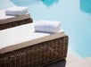 Two wicker lounge chairs with white cushions and folded towels are beside a clear blue swimming pool.