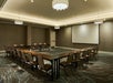 Empty conference room with U-shaped table arrangement, chairs, a large projector screen, and patterned carpet.