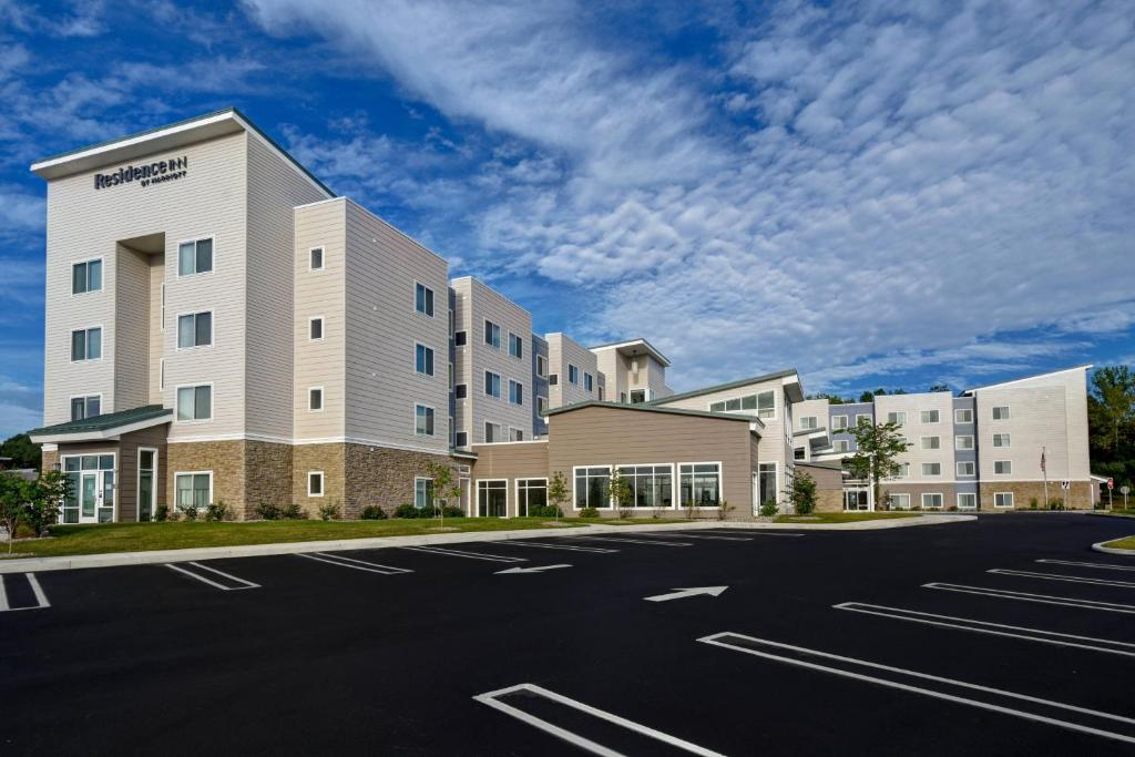 Four-story hotel with beige siding and stone accents, surrounded by an empty parking lot, under a sky filled with clouds.
