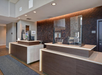 A modern hotel reception area with two wooden front desks, protective screens, and a textured wall in the background.