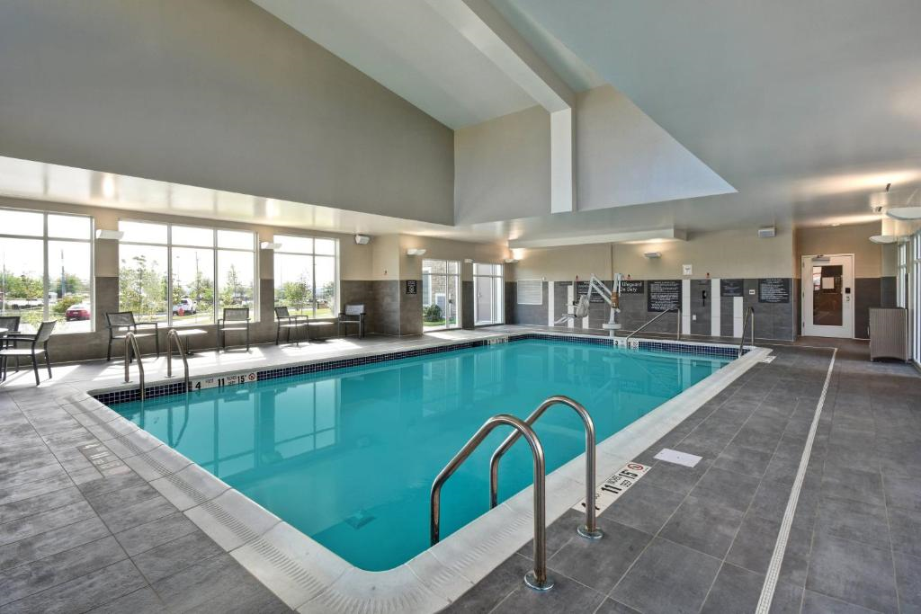 Indoor swimming pool with clear water surrounded by gray tiled flooring. Windows on one side provide natural light. Stairs and handrails give access to the pool.