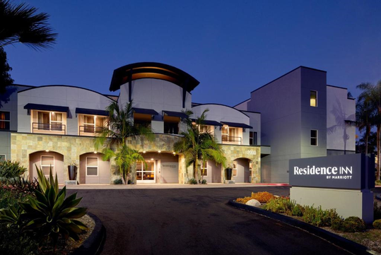 Exterior view of a Residence Inn by Marriott hotel with palm trees and lit signage at dusk.