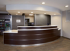 A modern hotel reception desk with dark wood and white accents. The area is well-lit, with a sign labeled "Lobby." Nearby shelves display snacks and beverages.