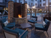 Outdoor seating area with four chairs around a fire pit, next to a pool in a courtyard setting with surrounding buildings.