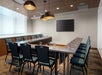 Conference room with a U-shaped table arrangement, empty chairs, glasses of water, ceiling lights, and a wall-mounted flat-screen TV.