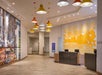 Modern hotel lobby with colorful hanging lamps, a wall mural on the left, a bright yellow textured panel on the right, and a reception desk with three computer stations.