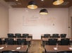 A classroom with several rows of empty desks and chairs, a whiteboard with mathematics graphs and equations, and three overhead lights. Glasses are placed on each desk.