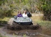 Two women in their Mucky Duck vehicle splash through muddy water