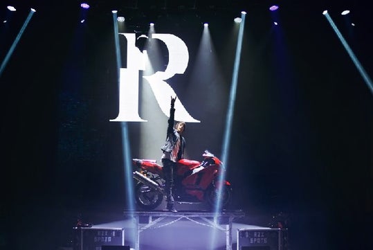 On top of a red motorcyle, Reza displays the rock symbol with his hand