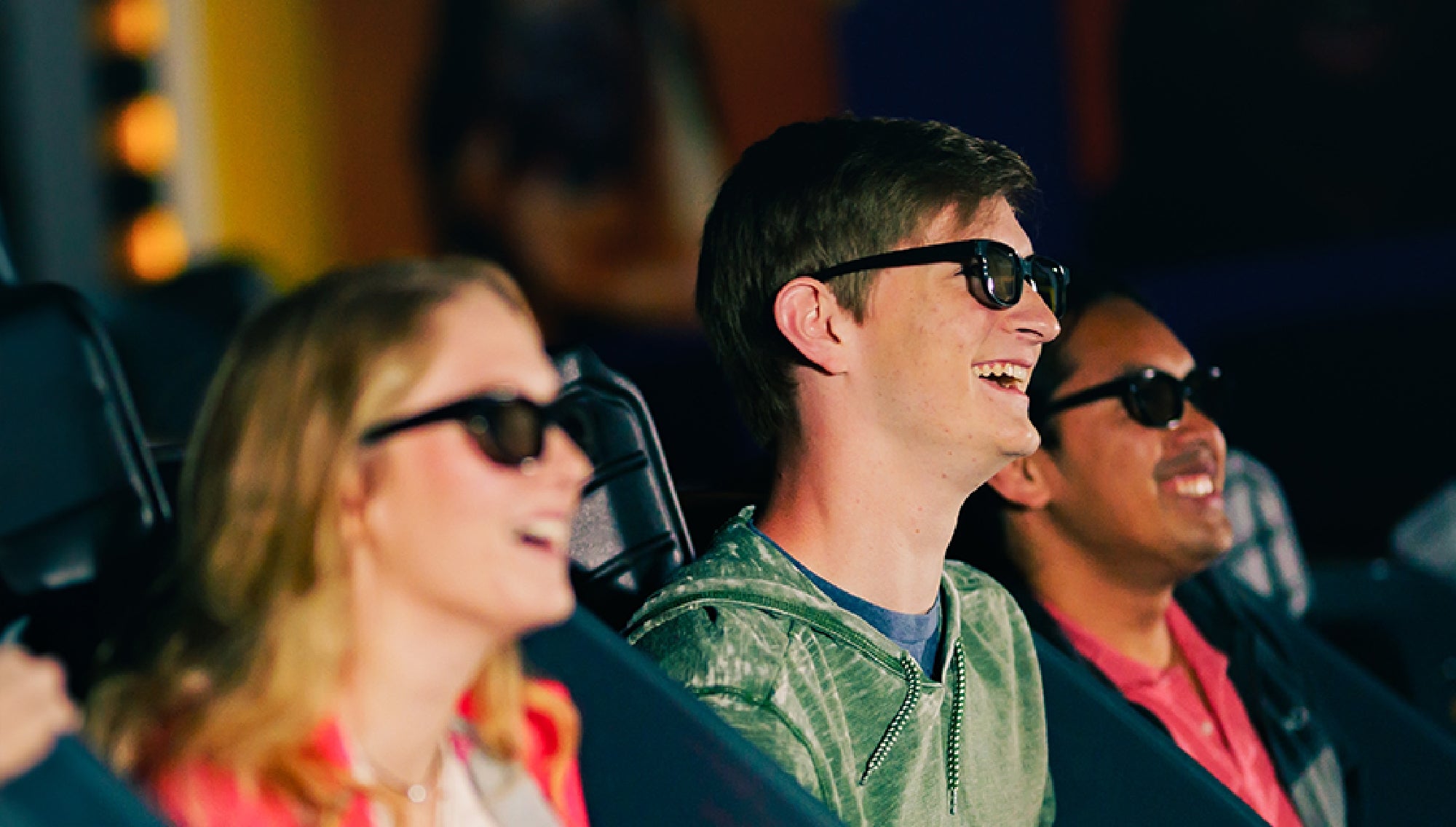 Three people wearing 3D glasses sit in a theater, smiling and enjoying the show.