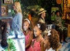Three children in matching dresses smile at a museum exhibit. Two adults, one in a safari outfit, are in the background.