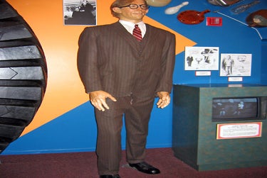 A very tall wax man in a brown suit and glasses with diagrams and old photos on the wall around him at Ripley's Believe It or Not! Orlando Odditorium.