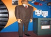 A very tall wax man in a brown suit and glasses with diagrams and old photos on the wall around him at Ripley's Believe It or Not! Orlando Odditorium.
