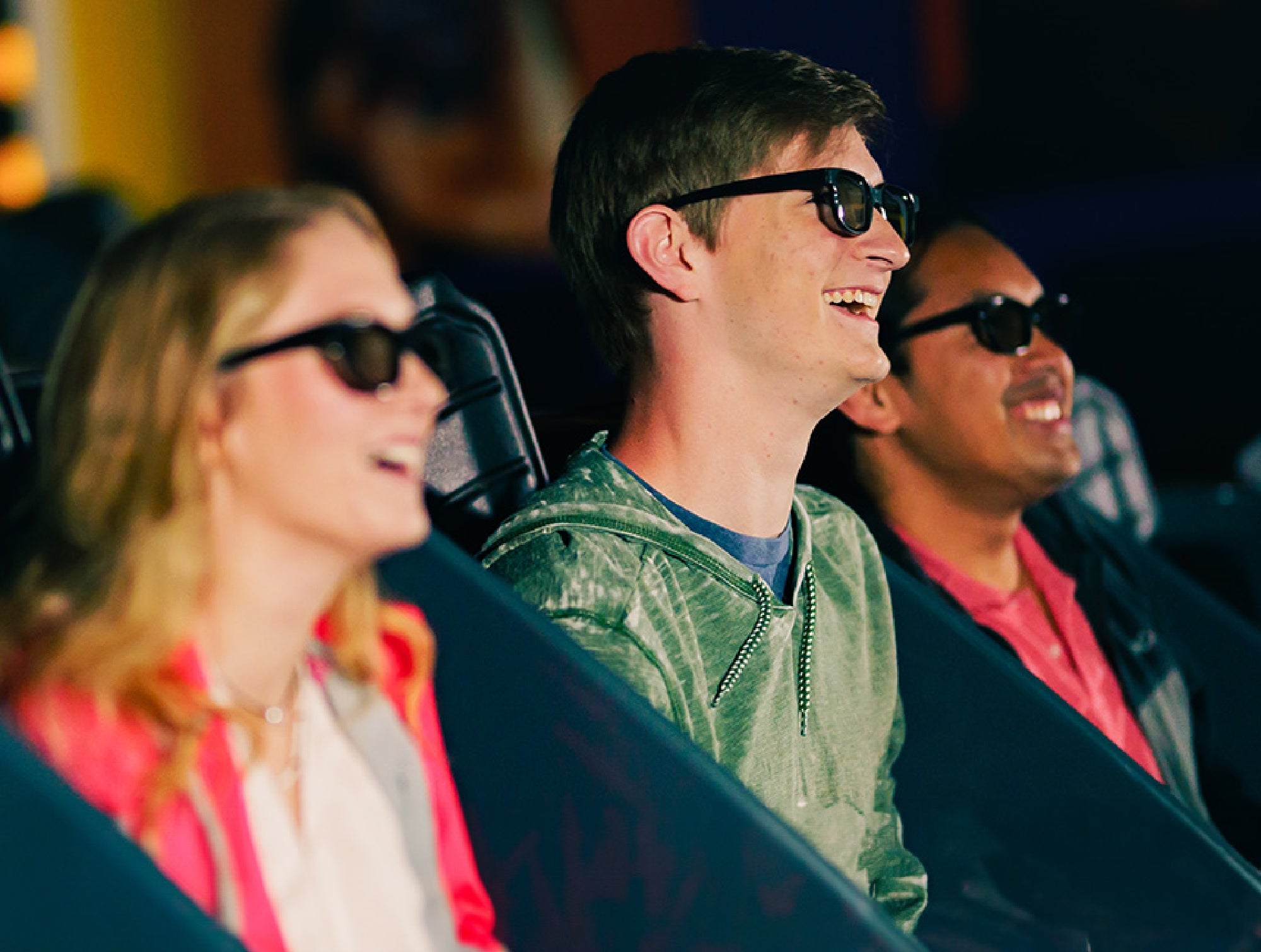 Three people wearing 3D glasses are seated and smiling, enjoying a movie or event indoors.