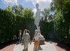 A group of people admire a large white statue in an outdoor setting surrounded by greenery and trees. One couple, holding hands, look up at the statue.