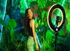 Girl in a black shirt and blue jeans posing with a greenery background with w ring light pointed at her at Ripley's Selfie Studio.