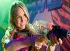 A blonde woman wearing a vest and holding up a laser gun while smiling at Ripley's Super Fun Park.