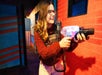 A woman in a red sweater and glasses smiling while playing laser tag at Ripley's Super Fun Park.