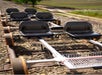 A small rail cart with two rows of seats on train tracks, surrounded by gravel and fields in the background.