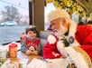 A child smiles at a person dressed as Santa Claus while sitting at a decorated table on a train during the holiday season.