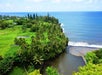 A lush green coastline with palm trees overlooks a river flowing into the ocean under a partly cloudy sky.