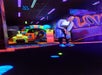 A person playing mini-golf indoors with neon lights and colorful decorations in the background.
