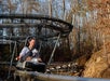 Person smiling while riding a single-seat roller coaster in a wooded area.