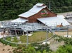 A mountain coaster track curves in front of a large wooden building labeled "Rocky Top Mountain Coaster," with trees and a road in the background.