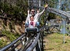 A man and a young girl ride a roller coaster cart on a metal track outdoors; the man raises his arms and smiles while the girl sits in front, both appearing excited.