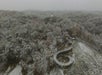 Aerial view of a snow-covered forested hill with a winding elevated walkway forming a loop near the center.