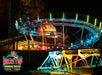 A brightly lit mountain coaster track at night with colorful lights, trees in the background, and a Rocky Top Mountain Coaster logo in the lower left corner.