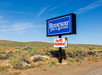 Sign for Rodeway Inn & Suites in a desert landscape offers free WiFi and breakfast. Blue sky and sparse vegetation in the background.